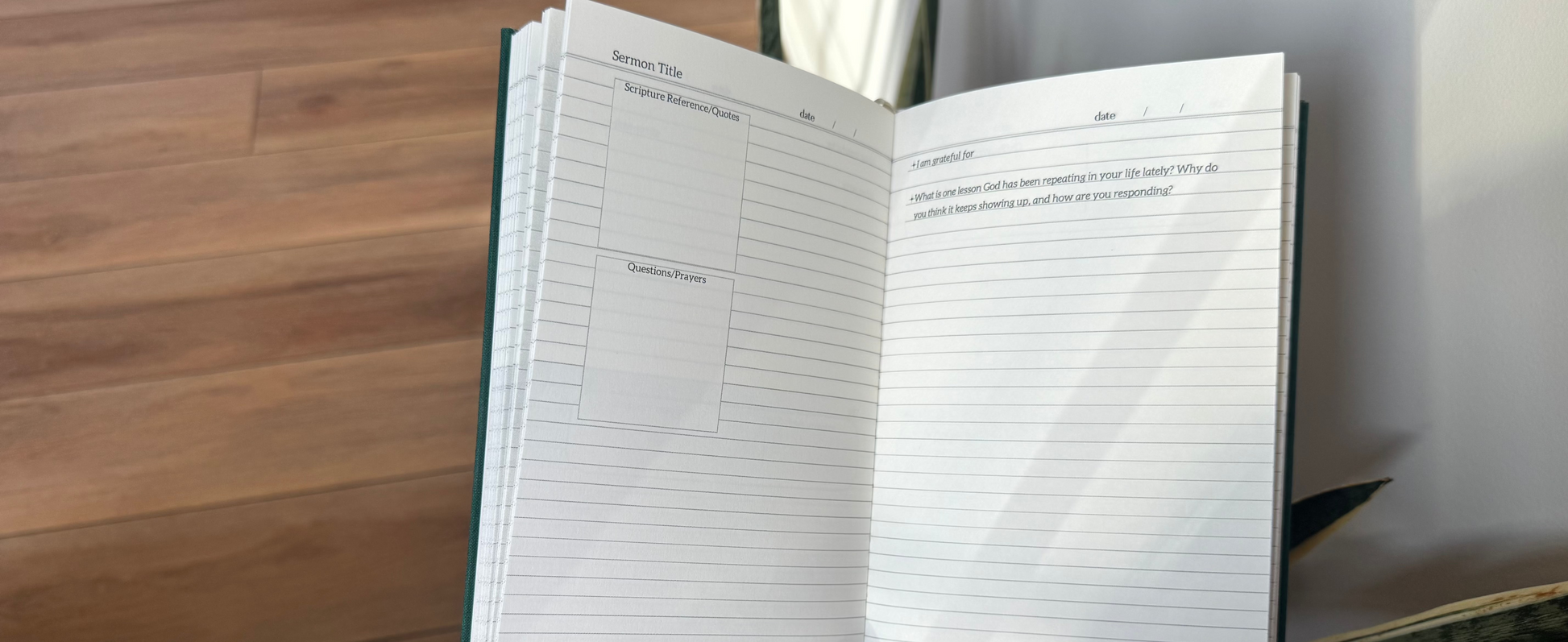 Hand holding an open notebook with lined pages on a wooden floor.